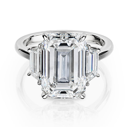 Luxurious three stone ring featuring a 7.57 carat emerald cut center diamond of H color and VS2 clarity, flanked by trapezoid cut diamonds in a handmade platinum setting. Ideal for a significant gift or personal collection.